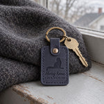 Navy Hurry Home keychain on car keys beside a front window at dusk