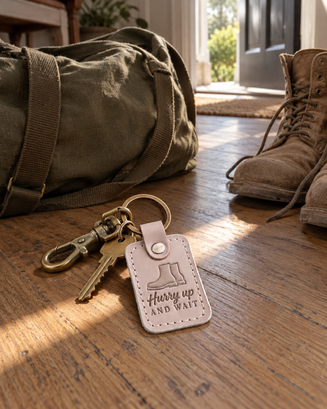 Hurry up and Wait keychain in soft gray leather on a set of keys beside a coffee mug on a workbench