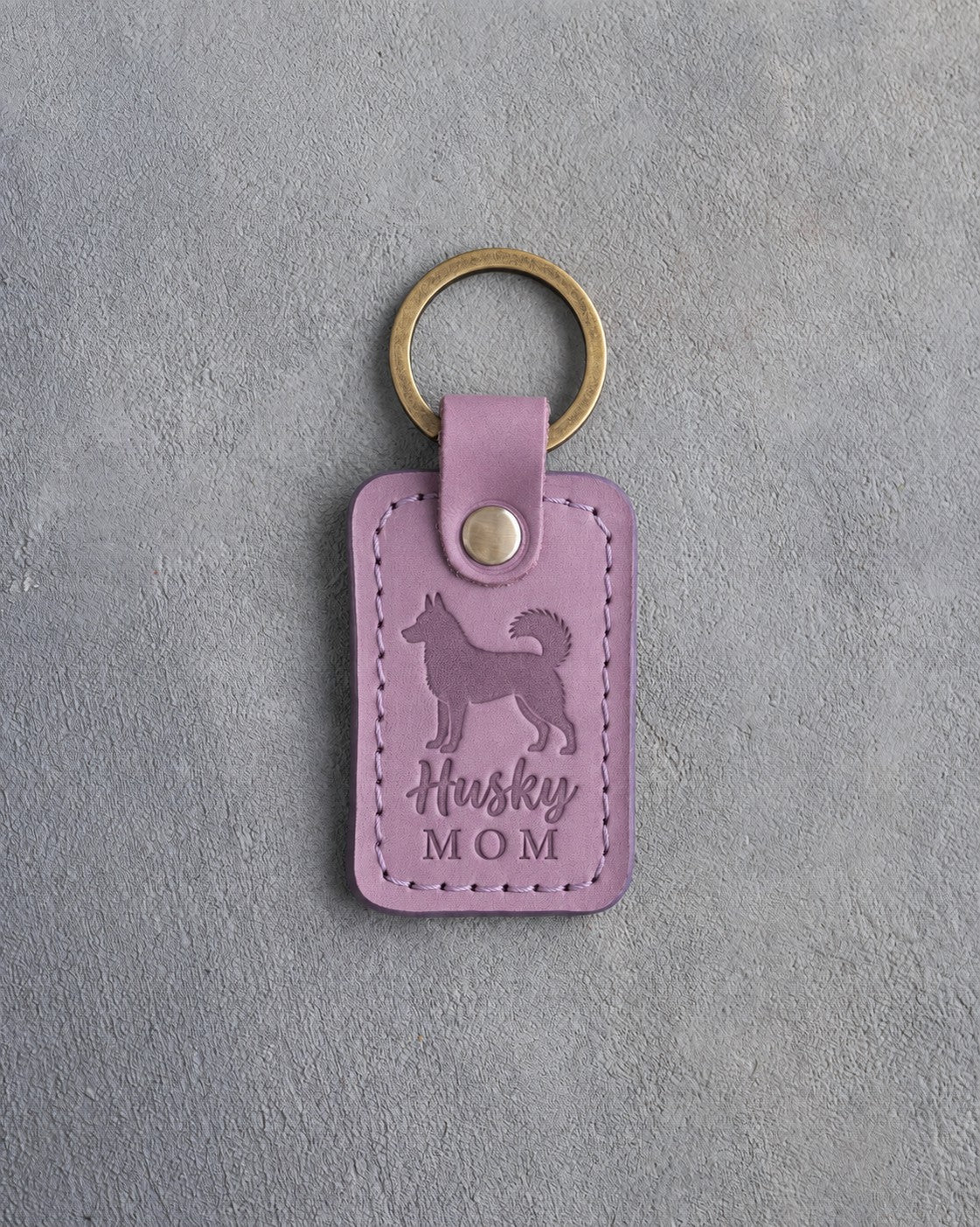 Lilac leather keychain debossed with a Siberian Husky silhouette and the words Husky MOM, on gray concrete