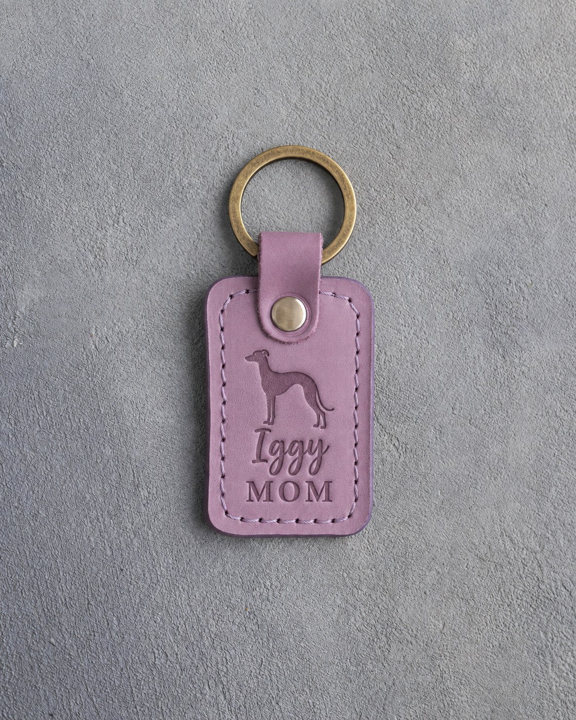 Lilac leather keychain debossed with an Italian Greyhound silhouette and the words Iggy MOM, on gray concrete