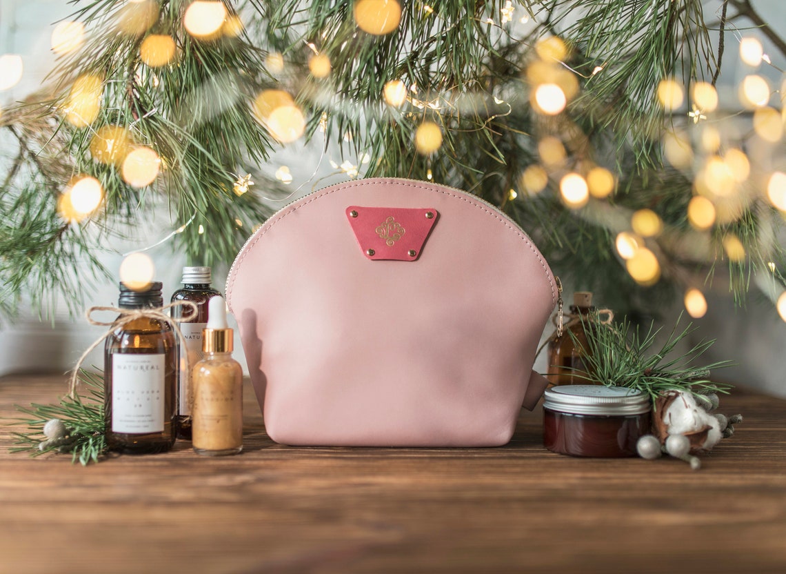 Blush round leather makeup bag with skincare bottles under a softly lit tree