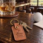 Inside the Leather keychain in caramel leather lying on a putting green beside a putter grip