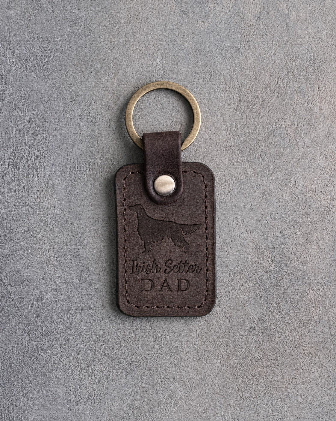 Dark espresso leather keychain debossed with an Irish Setter silhouette and the words Irish Setter DAD, on gray concrete