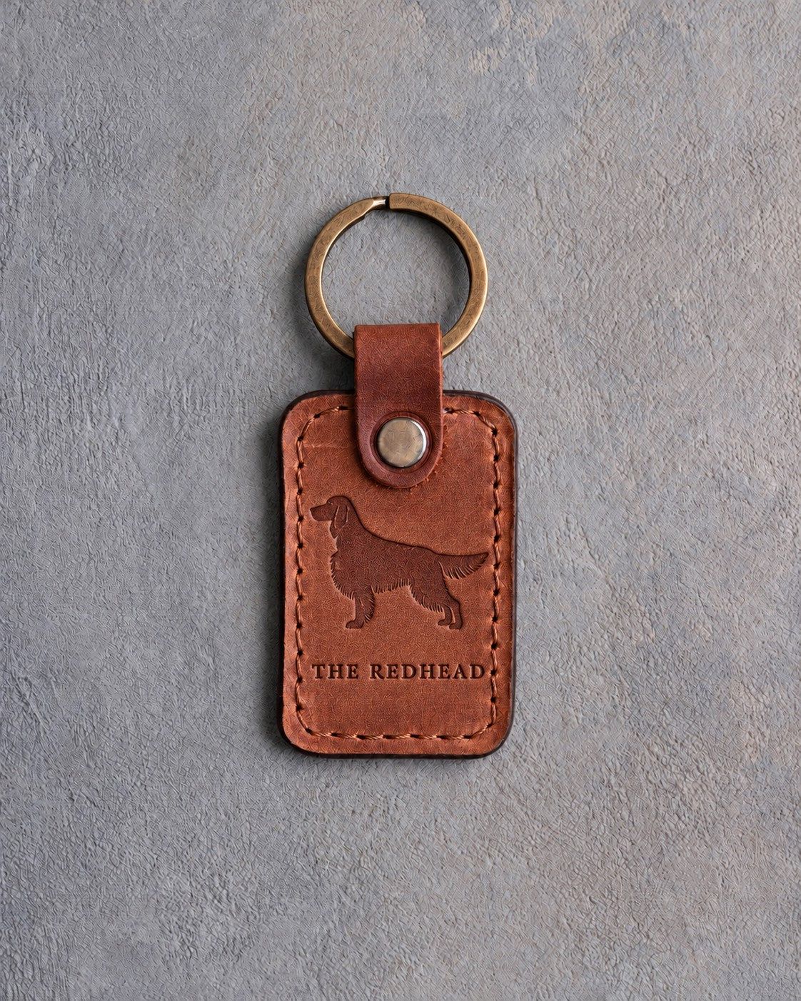 Arizona tan leather keychain debossed with an Irish Setter silhouette above THE REDHEAD, on gray concrete