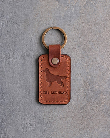 Arizona tan leather keychain debossed with an Irish Setter silhouette above THE REDHEAD, on gray concrete