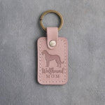 Blush pink leather keychain debossed with an Irish Wolfhound silhouette and the words Wolfhound MOM, on gray concrete