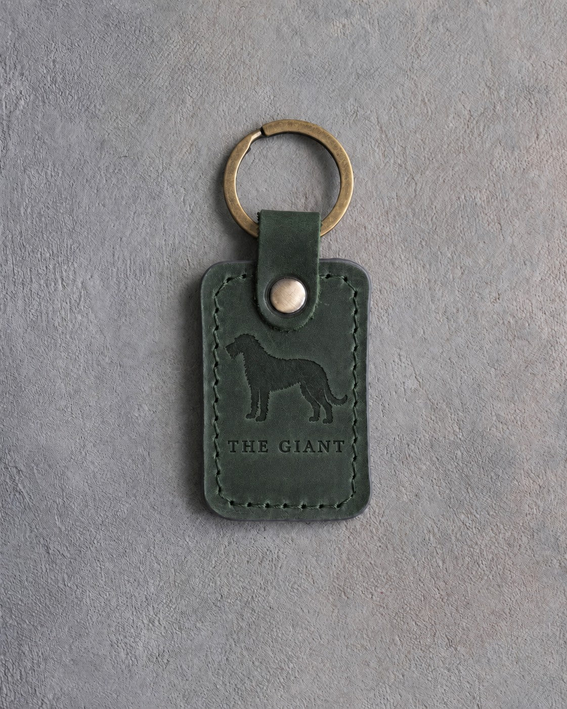 Forest green leather keychain debossed with an Irish Wolfhound silhouette above THE GIANT, on gray concrete