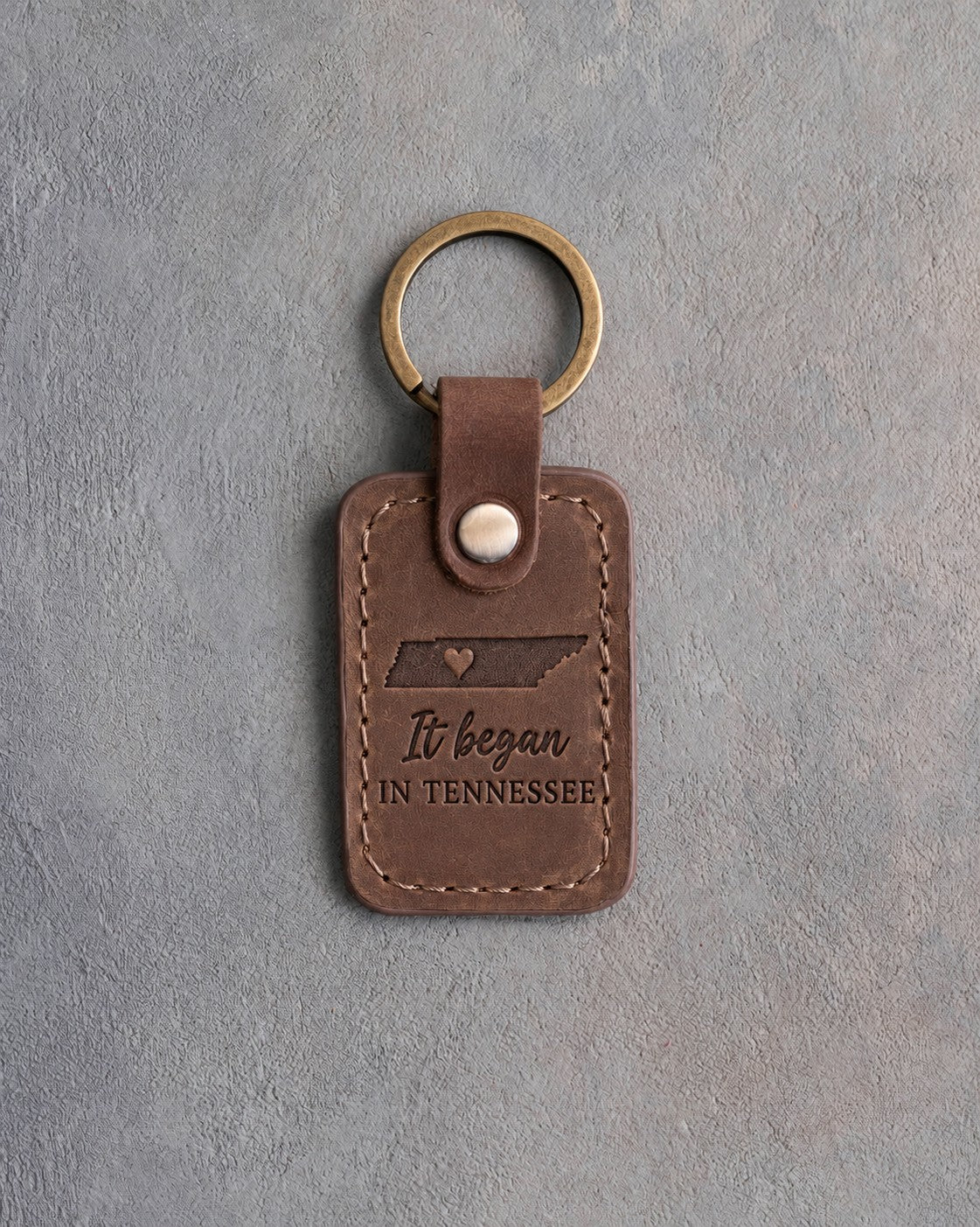 Sicilian brown leather keychain debossed with the Tennessee state outline and a heart at Nashville above It began IN TENNESSEE, on gray concrete