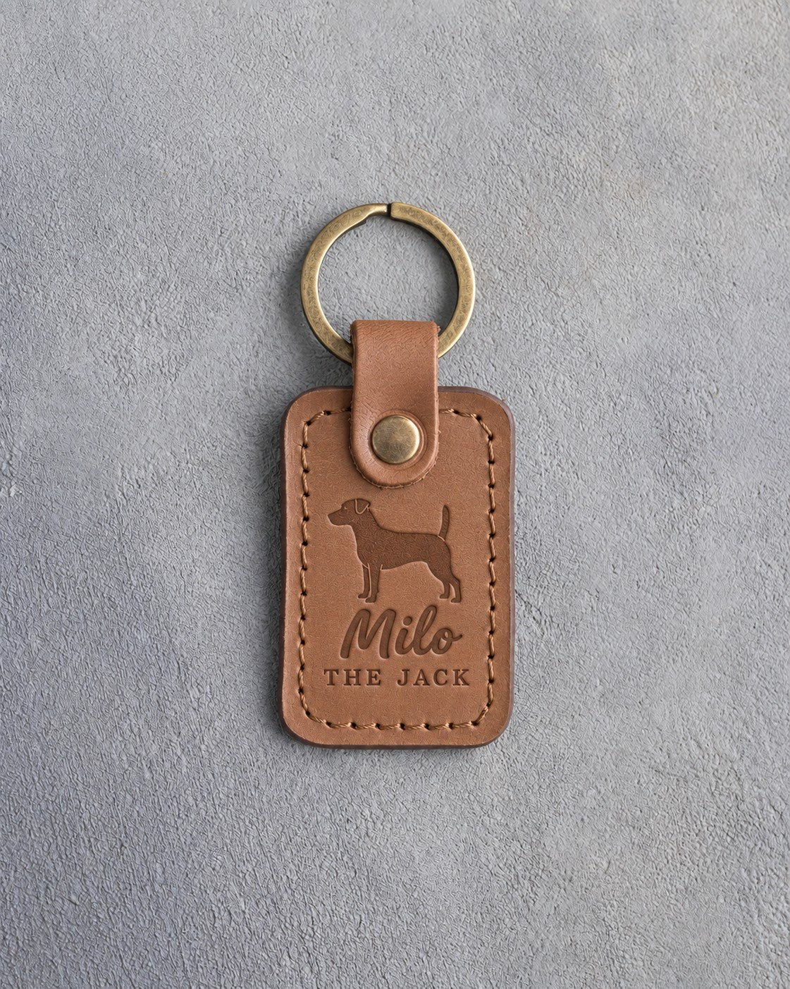 Caramel leather keychain debossed with a Jack Russell terrier above the name Milo and THE JACK, on gray concrete