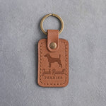 Caramel leather keychain debossed with a Jack Russell terrier above Jack Russell and TERRIER, on gray concrete