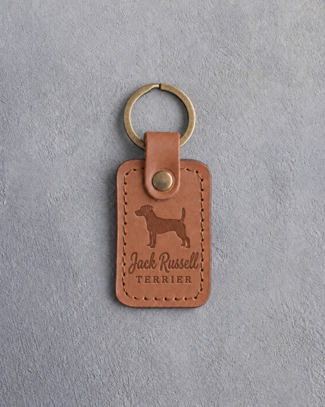 Caramel leather keychain debossed with a Jack Russell terrier above Jack Russell and TERRIER, on gray concrete