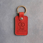 Poppy red leather keychain debossed with two interlocked wedding rings above the words Just MARRIED, on gray concrete