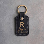 Black leather keychain with a gold foil Walking R ranch brand above Keys to and THE RANCH, on gray plaster
