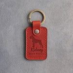 Poppy red leather keychain debossed with a Boxer silhouette and the words Kidney BEAN WIGGLE, on gray concrete