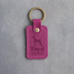 Fuchsia leather keychain debossed with a miniature pinscher and the words King of TOYS, on gray concrete