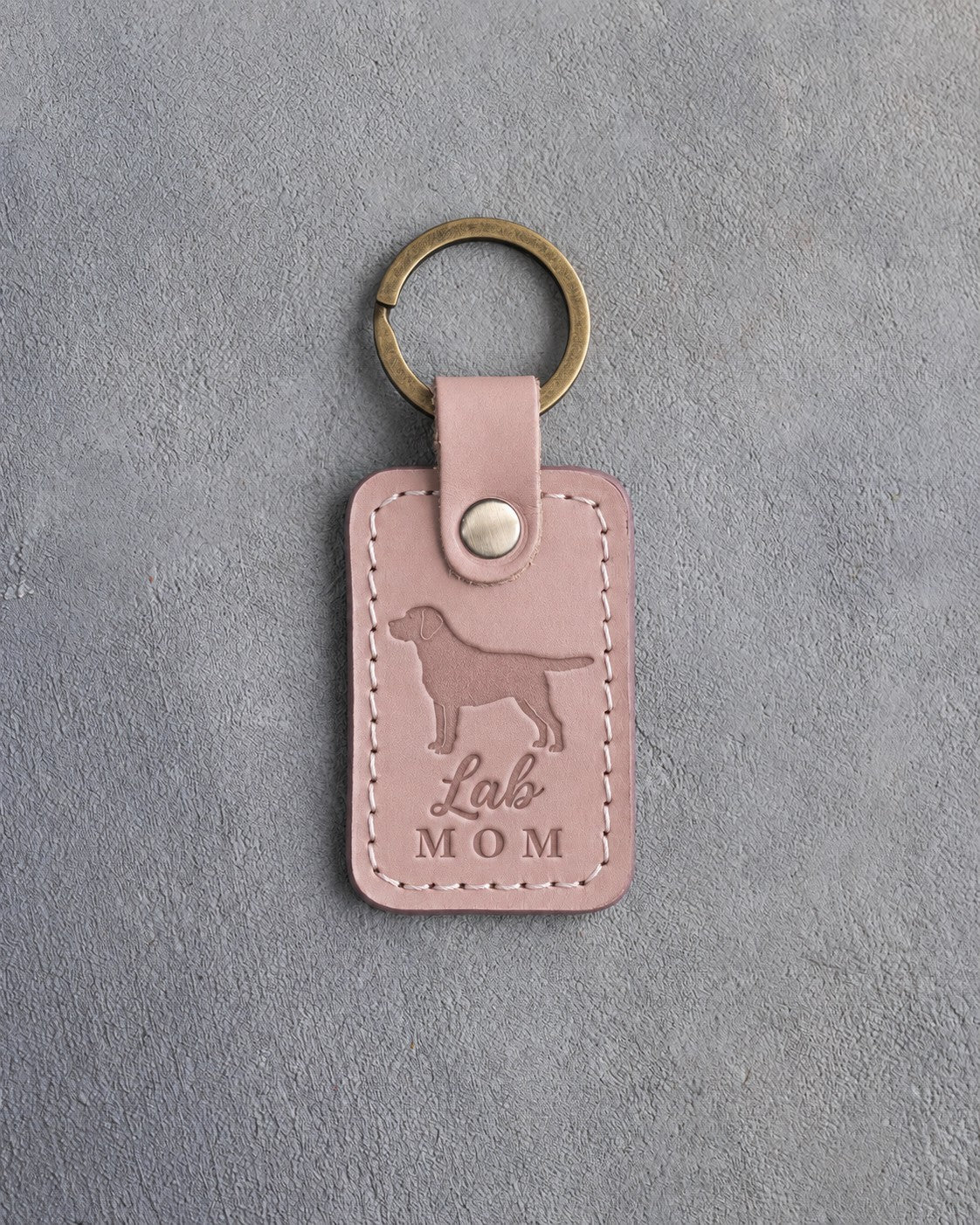 Blush pink leather keychain debossed with a Labrador Retriever silhouette and the words Lab MOM, on gray concrete