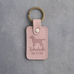 Blush pink leather keychain debossed with a Labradoodle silhouette and the words Labradoodle MOM, on gray concrete