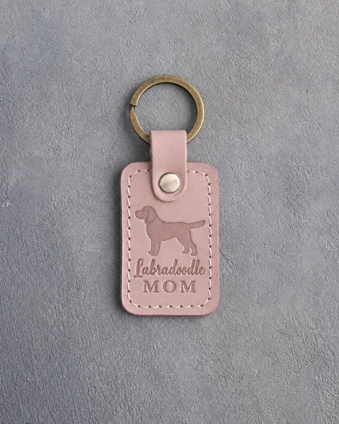 Blush pink leather keychain debossed with a Labradoodle silhouette and the words Labradoodle MOM, on gray concrete