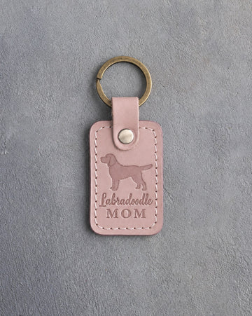 Blush pink leather keychain debossed with a Labradoodle silhouette and the words Labradoodle MOM, on gray concrete