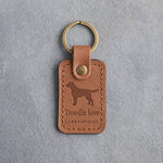 Caramel leather keychain debossed with a Labradoodle silhouette above Doodle love and LABRADOODLE, on gray concrete