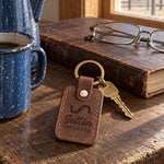 Sutton LAND & CATTLE keychain in Sicilian brown leather on a ranch house kitchen table beside an enamel coffee pot