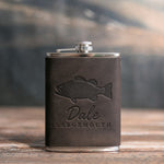 Dark espresso leather-wrapped hip flask debossed with a largemouth bass above Dale and LARGEMOUTH, on a wooden table
