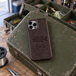 Dark espresso Dale LARGEMOUTH iPhone case in full-grain leather on the lid of an olive-green steel tackle box in a garage, lures in the trays behind