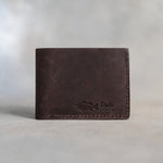 Closed dark espresso leather bifold wallet with a largemouth bass beside Dale and LARGEMOUTH pressed in the lower right corner, on gray plaster
