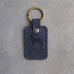 Blueberry navy leather keychain debossed with a Bernese mountain dog and the words Leans on EVERYONE, on gray concrete