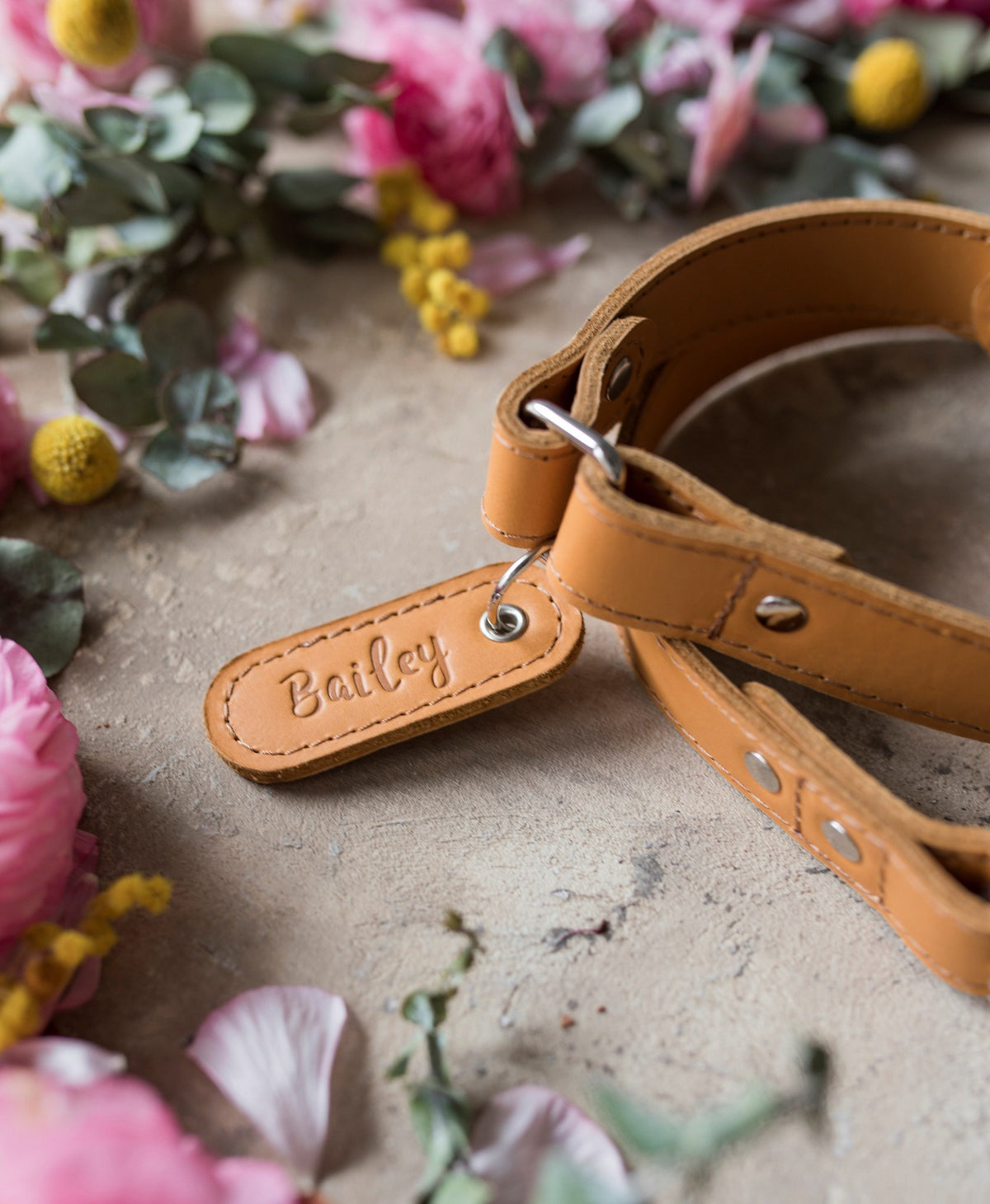 Close-up of a leather dog leash name tab with the name Bailey debossed in cursive