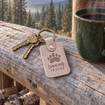Leave Only Tracks keychain in pale gray leather clipped to a daypack zipper on a dusty mountain trail