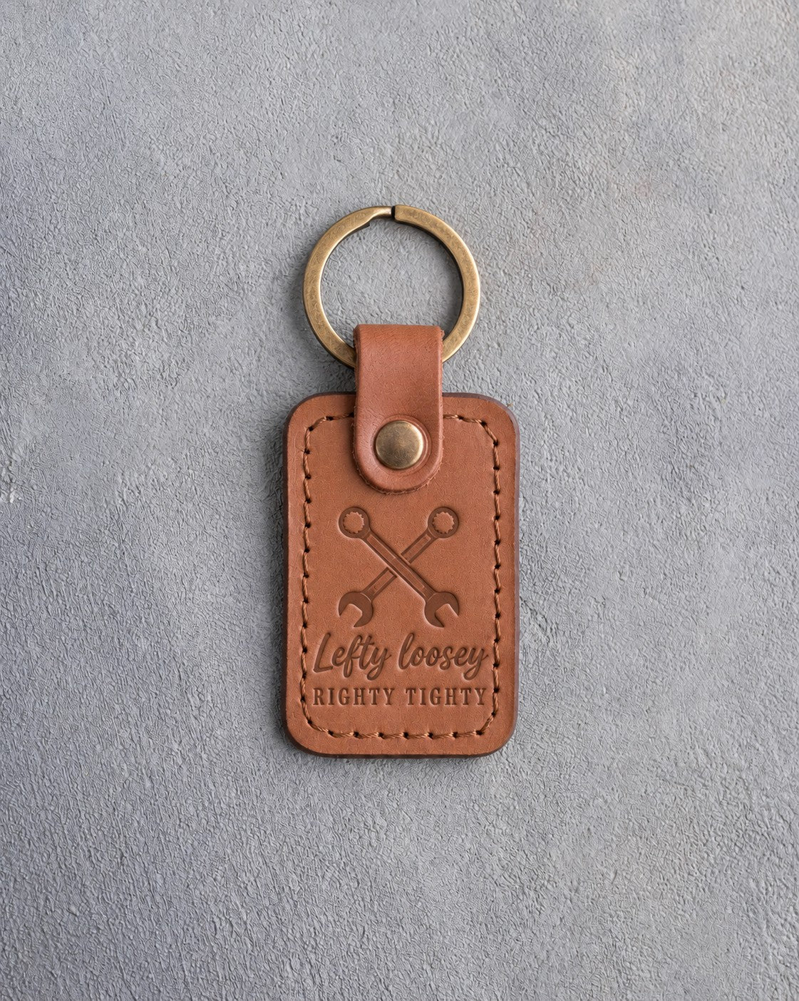 Caramel leather keychain debossed with crossed wrenches above the words Lefty loosey and RIGHTY TIGHTY, on gray plaster