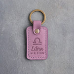 Lilac leather keychain debossed with the Libra zodiac glyph above Libra and AIR SIGN, on gray concrete