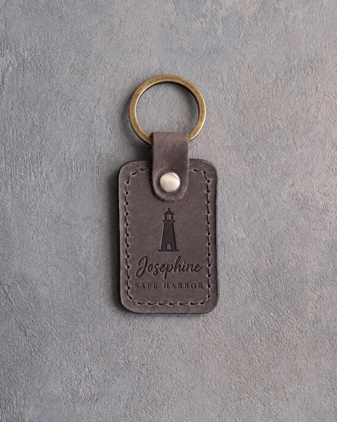 Country Gray leather keychain debossed with a lighthouse above Josephine and SAFE HARBOR, on gray plaster