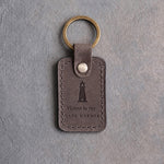 Country Gray leather keychain debossed with a lighthouse above Home is my and SAFE HARBOR, on gray concrete