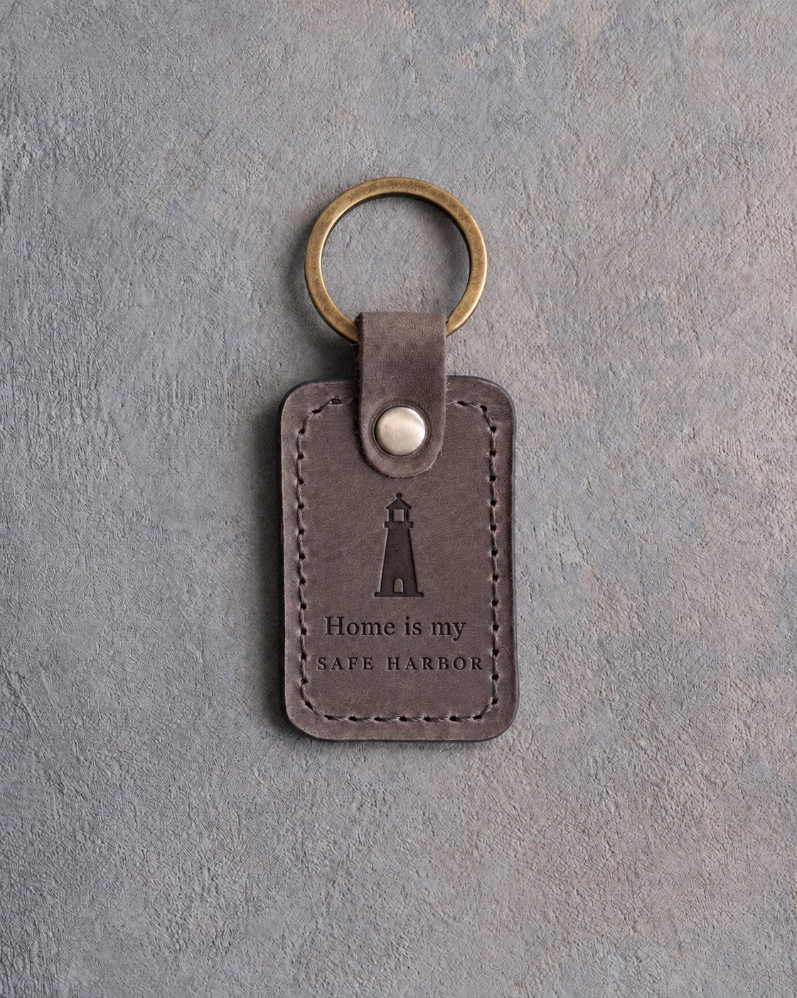 Country Gray leather keychain debossed with a lighthouse above Home is my and SAFE HARBOR, on gray concrete