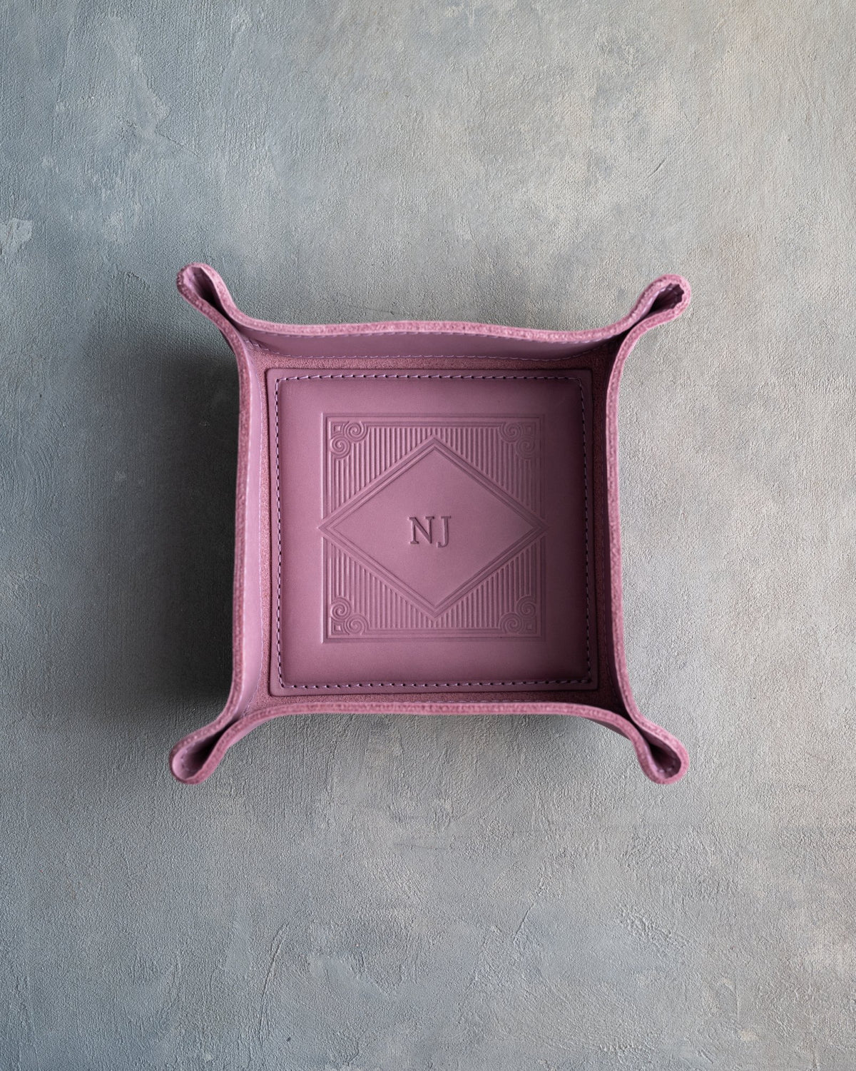 Lilac leather valet tray with snapped corners and the initials NJ pressed into the diamond frame, seen from above