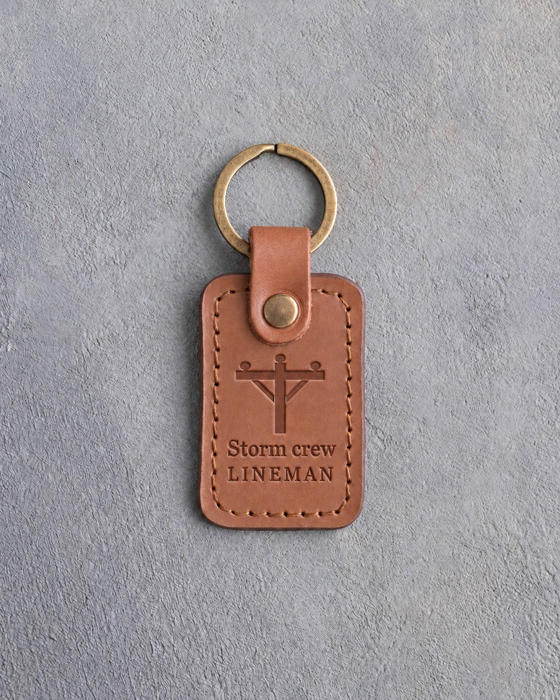 Caramel leather keychain debossed with a utility pole and crossarm above the words Storm crew and LINEMAN, on gray concrete