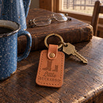 Caramel Little BUCKAROO keychain on a dark oak ranch kitchen table beside a speckled enamel coffee pot