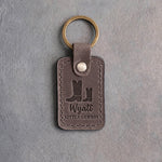 Country gray leather keychain debossed with a big and a small cowboy boot above the name Wyatt and LITTLE COWBOY, on gray plaster
