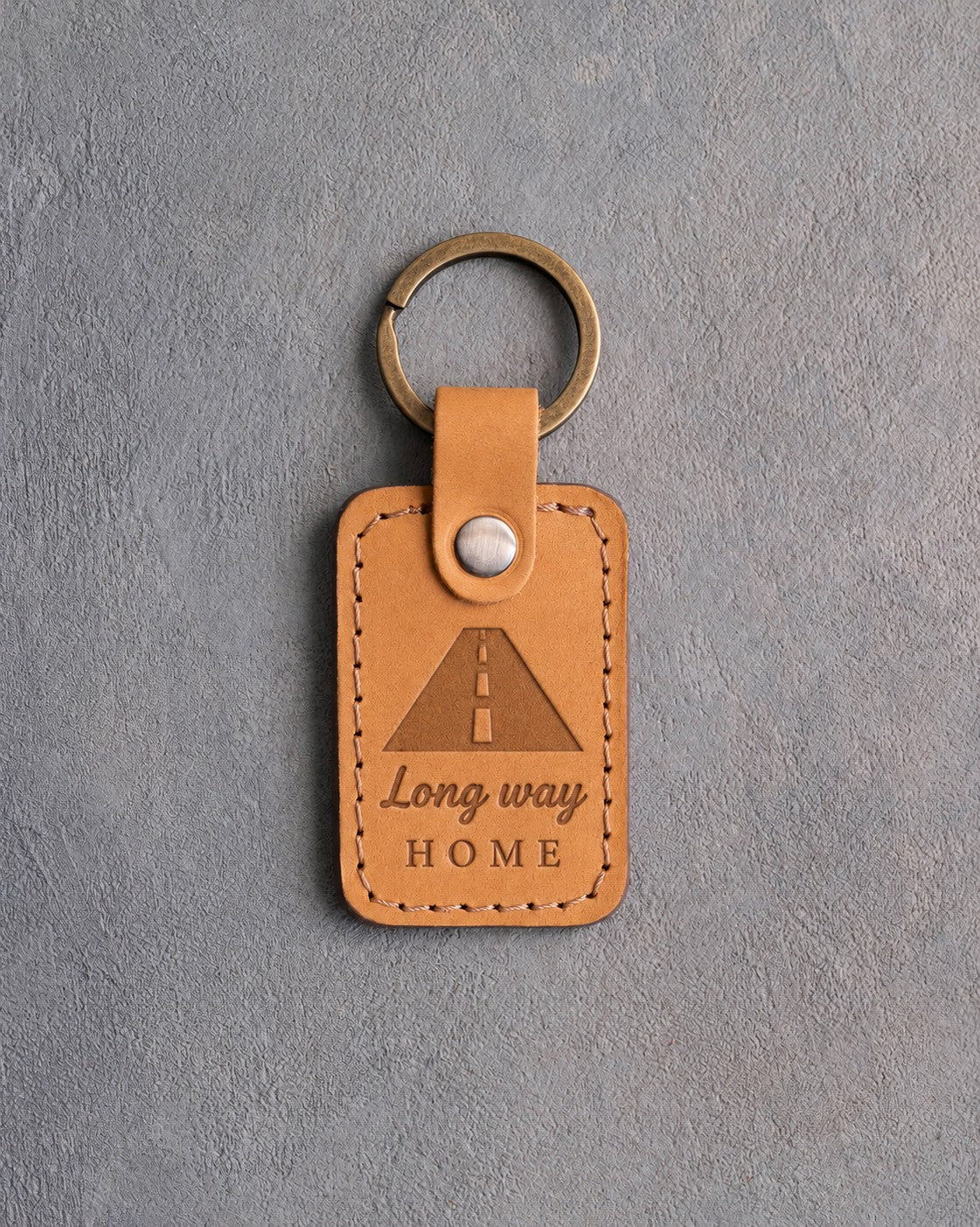 Golden tan leather keychain debossed with a road to the horizon above Long way and HOME