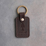 Dark espresso leather keychain debossed with a giant sequoia tree above Look up and SEQUOIA, on gray concrete