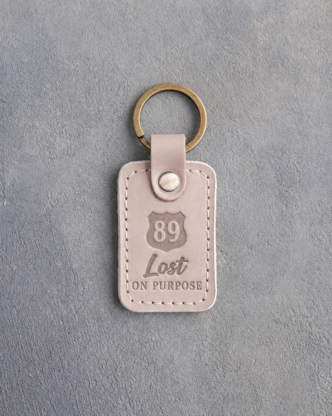 Gray sand leather keychain debossed with a route shield numbered 89 above Lost and ON PURPOSE