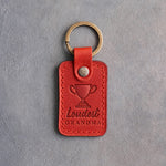 Poppy red leather keychain debossed with a trophy cup and the words Loudest GRANDMA, on gray plaster