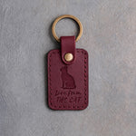 Sangria red leather keychain debossed with a cat looking up above the words Love from and THE CAT, on gray concrete
