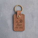 Caramel leather keychain debossed with a paw print on a signature line above Love and THE DOG, on gray concrete