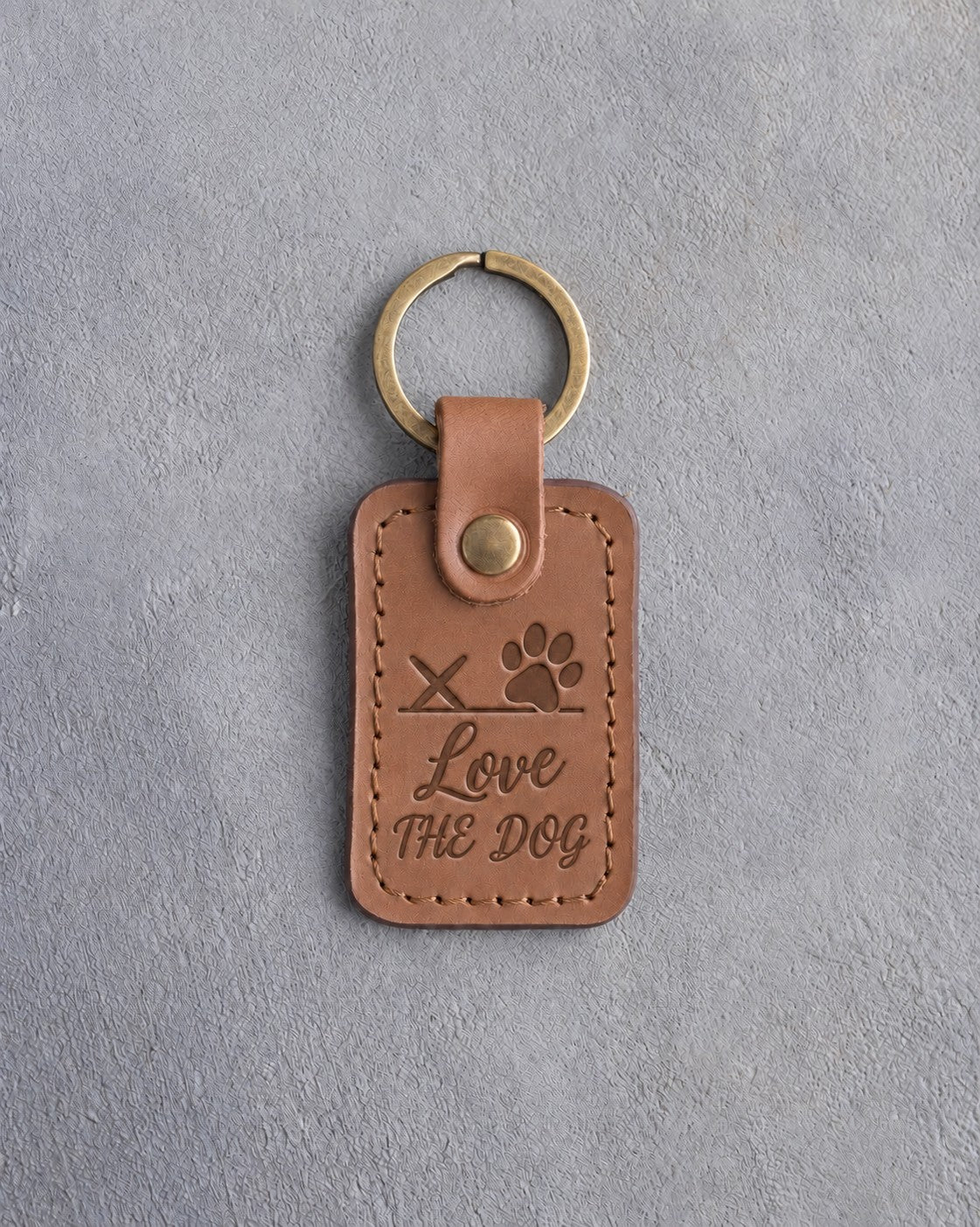 Caramel leather keychain debossed with a paw print on a signature line above Love and THE DOG, on gray concrete