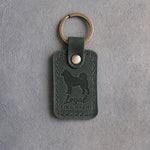 Forest green leather keychain debossed with an Akita and the words Loyal LIKE HACHI, on gray concrete