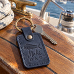 Blueberry Mahi DAD keychain in full-grain leather on the worn teak cockpit table of a sailboat beside a coiled white dock line
