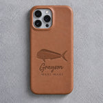Back of a caramel leather iPhone case debossed with a mahi mahi above Grayson and MAHI MAHI below the camera, on gray plaster